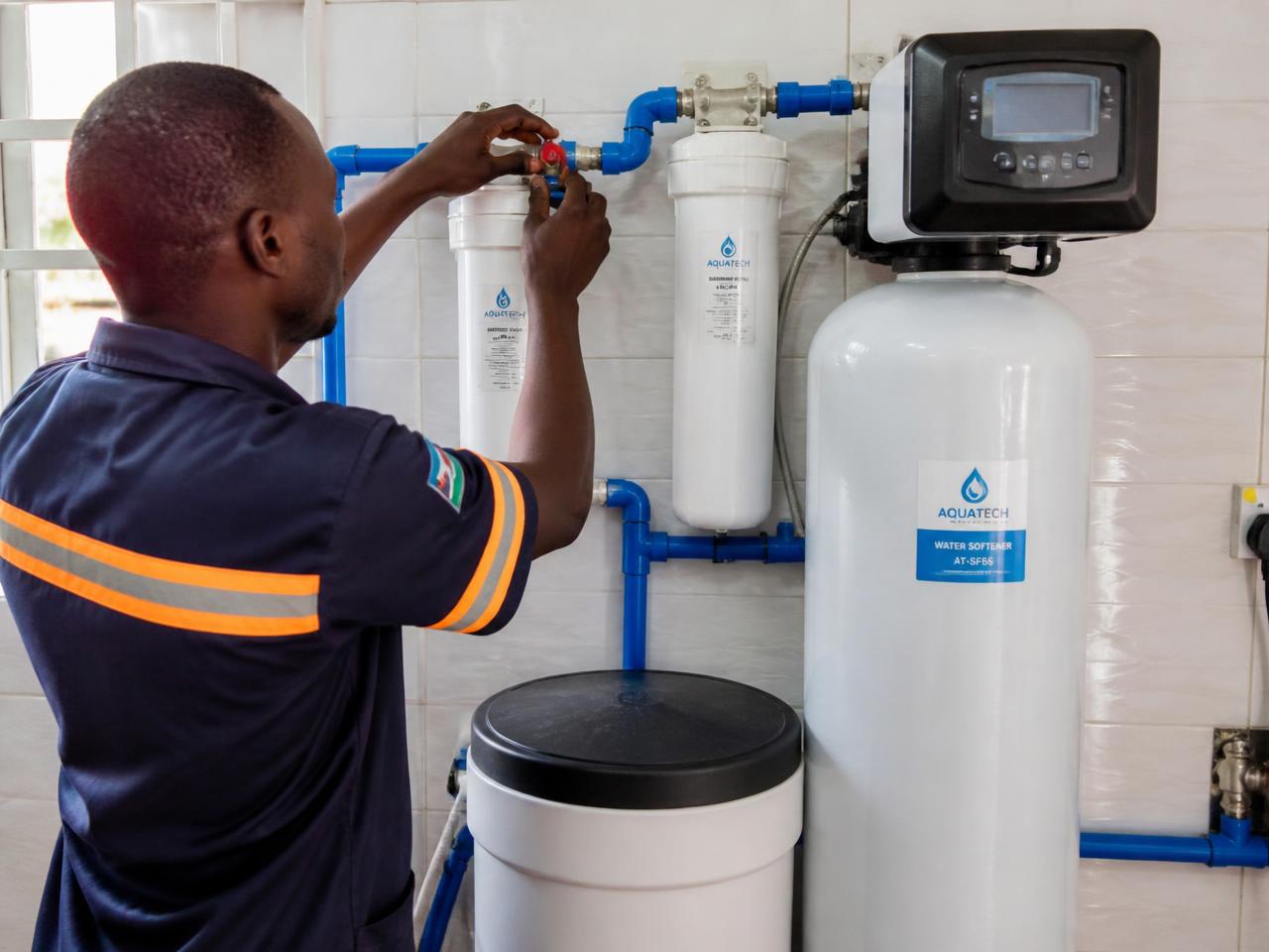 Ghanaian technician adjusting a valve on a home water filtration and softener installation